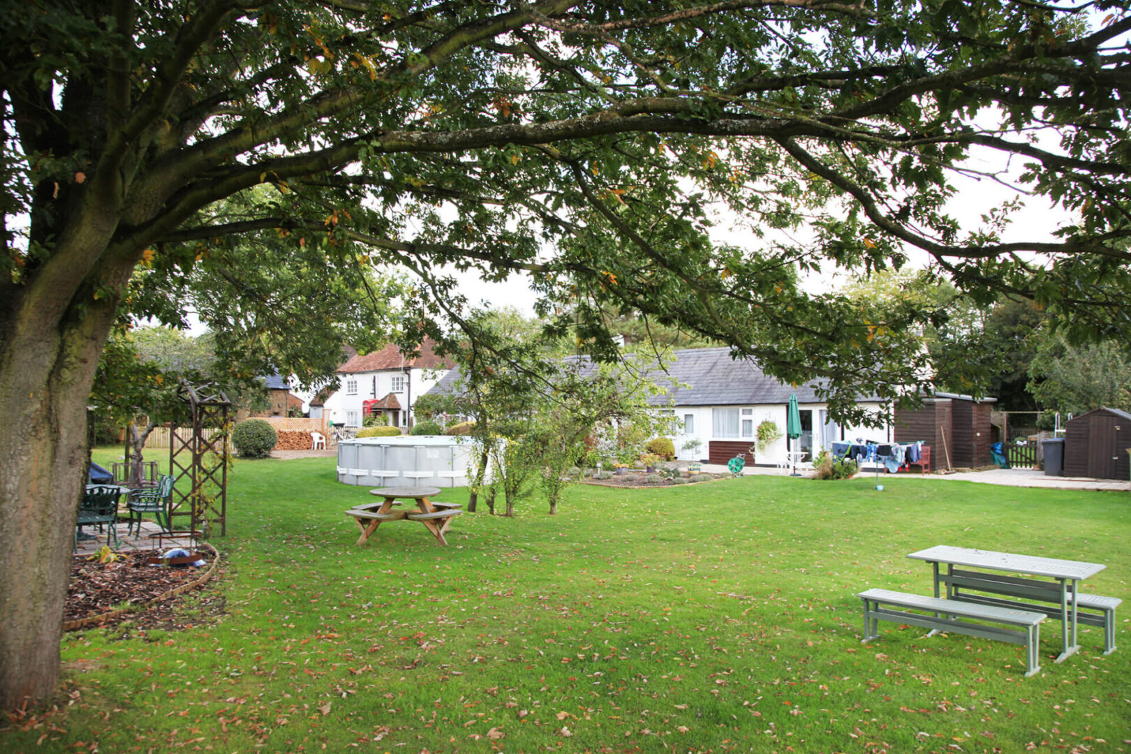 Pet-Friendly Cottages, Maidenhead | Sheephouse Manor Cottages garden view with drier pool benches and tables barbeque area, green grass and old big tree. autumn view