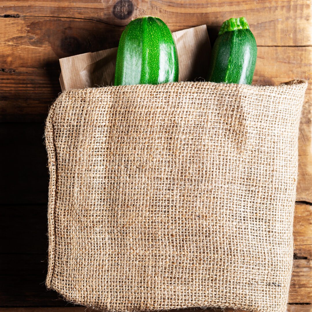 Courgettes in linen reusable bag. Choose less plastic when buying vegetables. Rustic wooden background
